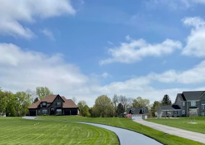A paved path curves through a grassy field with houses and trees under a partly cloudy blue sky, showcasing the quality of Expert Paving Solutions in Hanover MD.