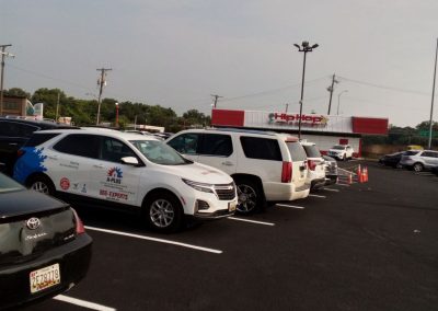 Cars parked in a lot on a sunny day, with a restaurant and trees visible in the background.
