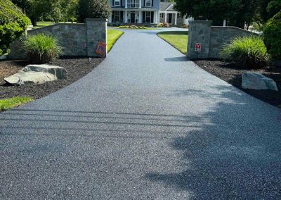 A wide driveway leads to a large house with a porch, surrounded by green lawns and trees.