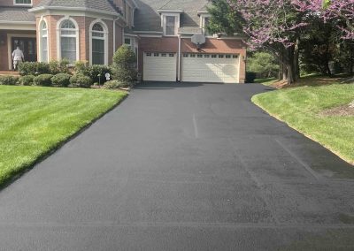 Freshly paved black driveway in front of a brick house, blocked off with yellow caution tape.
