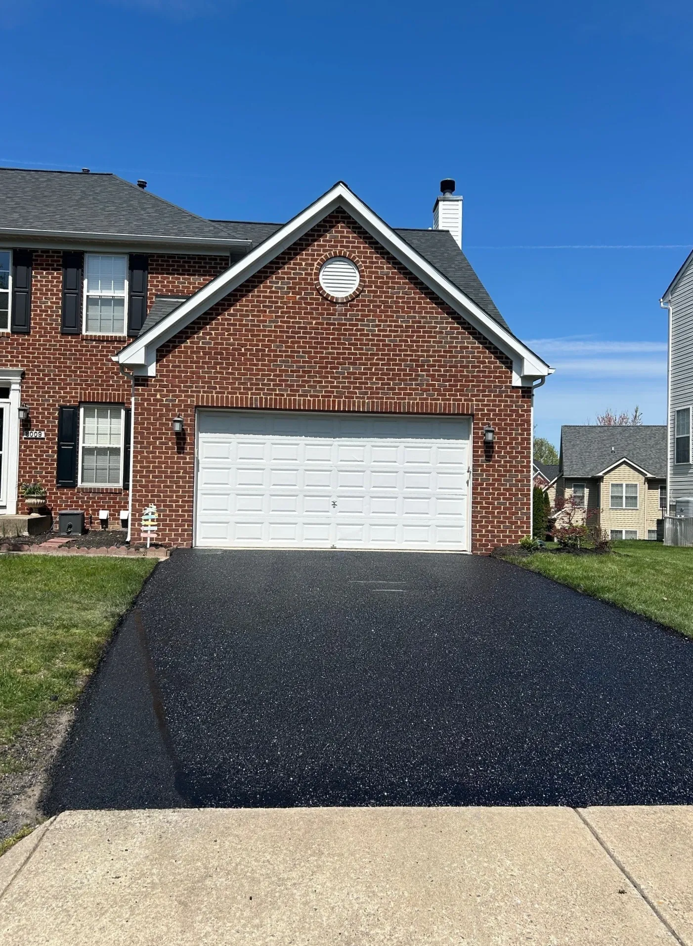 Paving 3 A newly paved black asphalt driveway leads to a brick house with a white garage door.