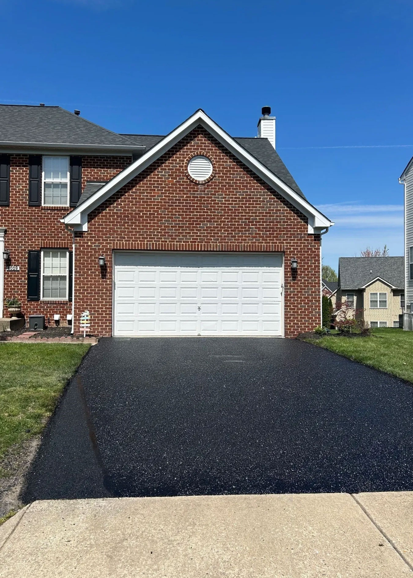 A two-car garage with a new black asphalt driveway in front of a brick suburban house.