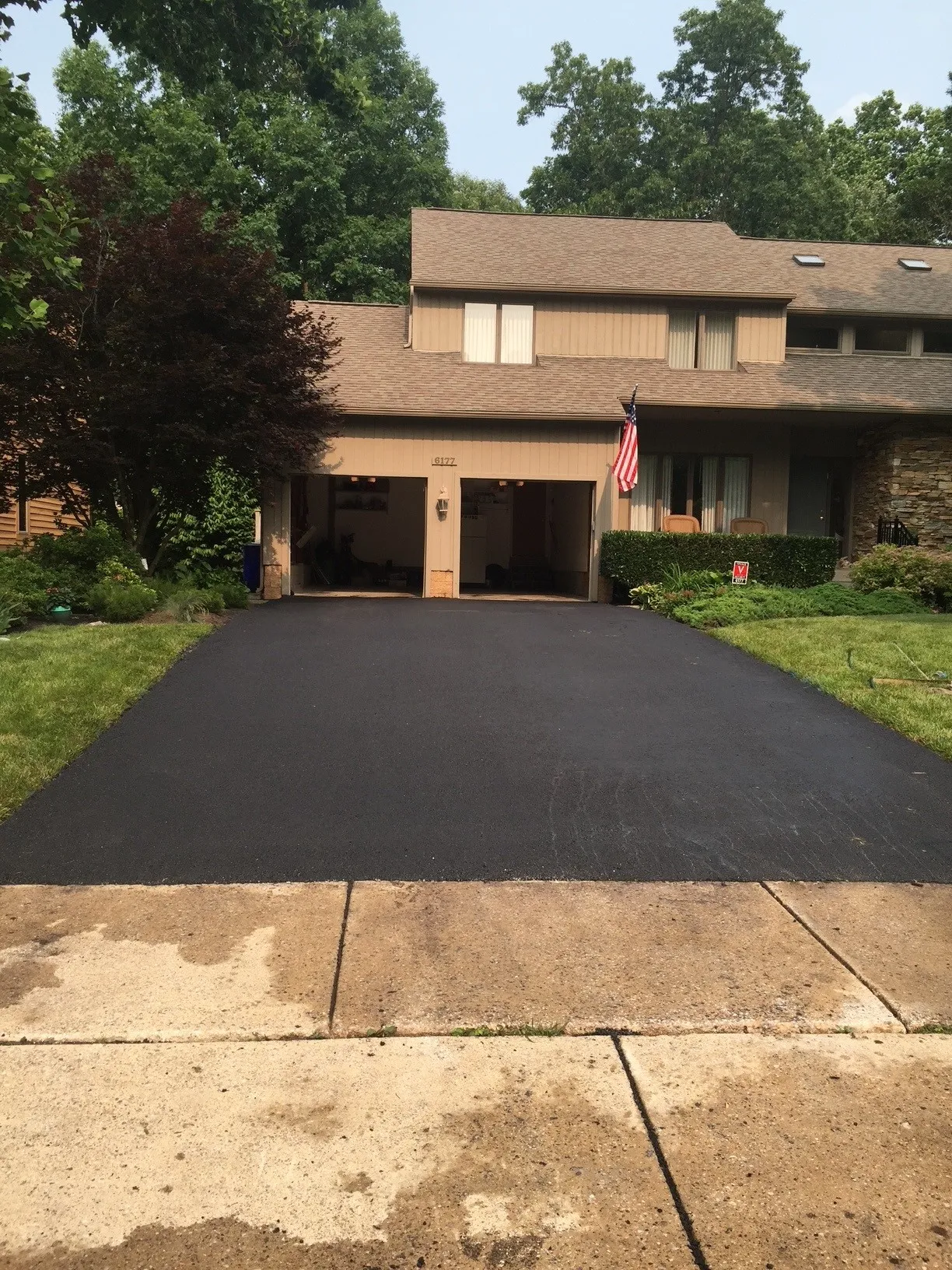 Paving Freshly paved black asphalt driveway in front of a suburban house with an American flag by the garage.
