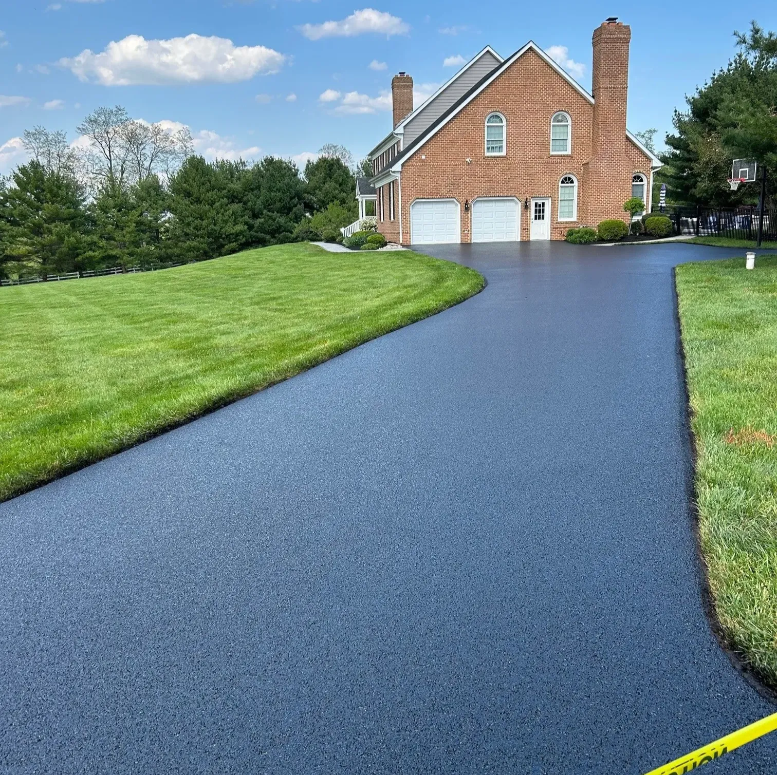 loc-1 Freshly paved black asphalt driveway leading to a brick house with a well-manicured green lawn.
