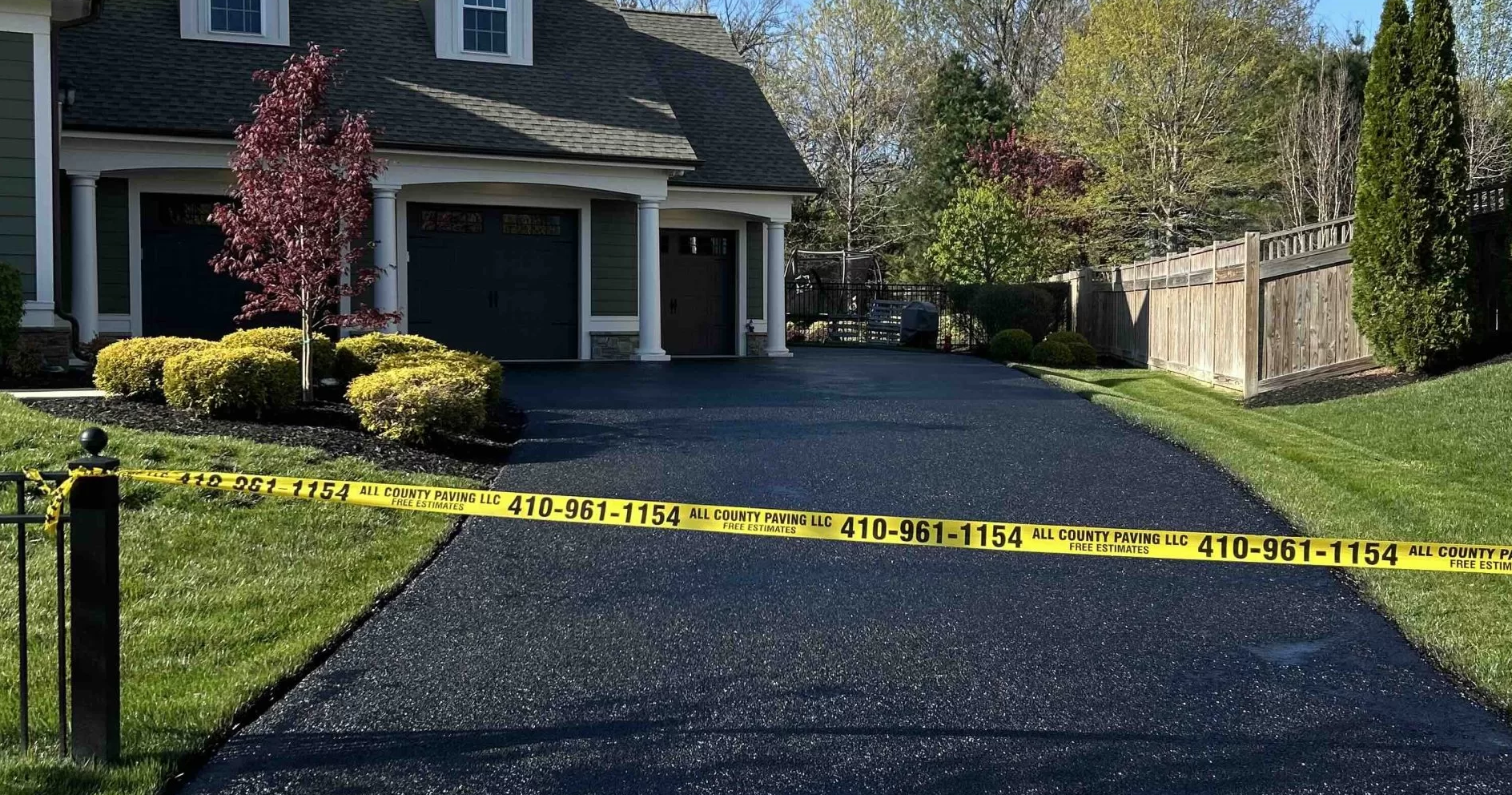Freshly paved driveway blocked by yellow caution tape, in front of a house with a garage and manicured lawn.